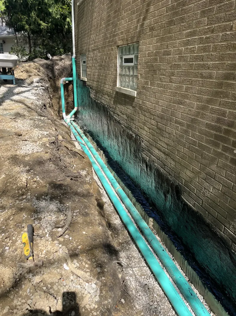 Foundation waterproofing work in progress beside a home